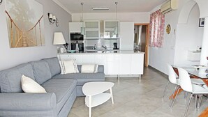 Un soggiorno moderno con un divano grigio, un tavolino da caffè bianco e un'area pranzo con sedie bianche e un tavolo in vetro.