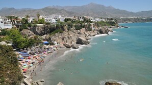 Una località costiera con spiaggia rocciosa, mare cristallino e montagne sullo sfondo.