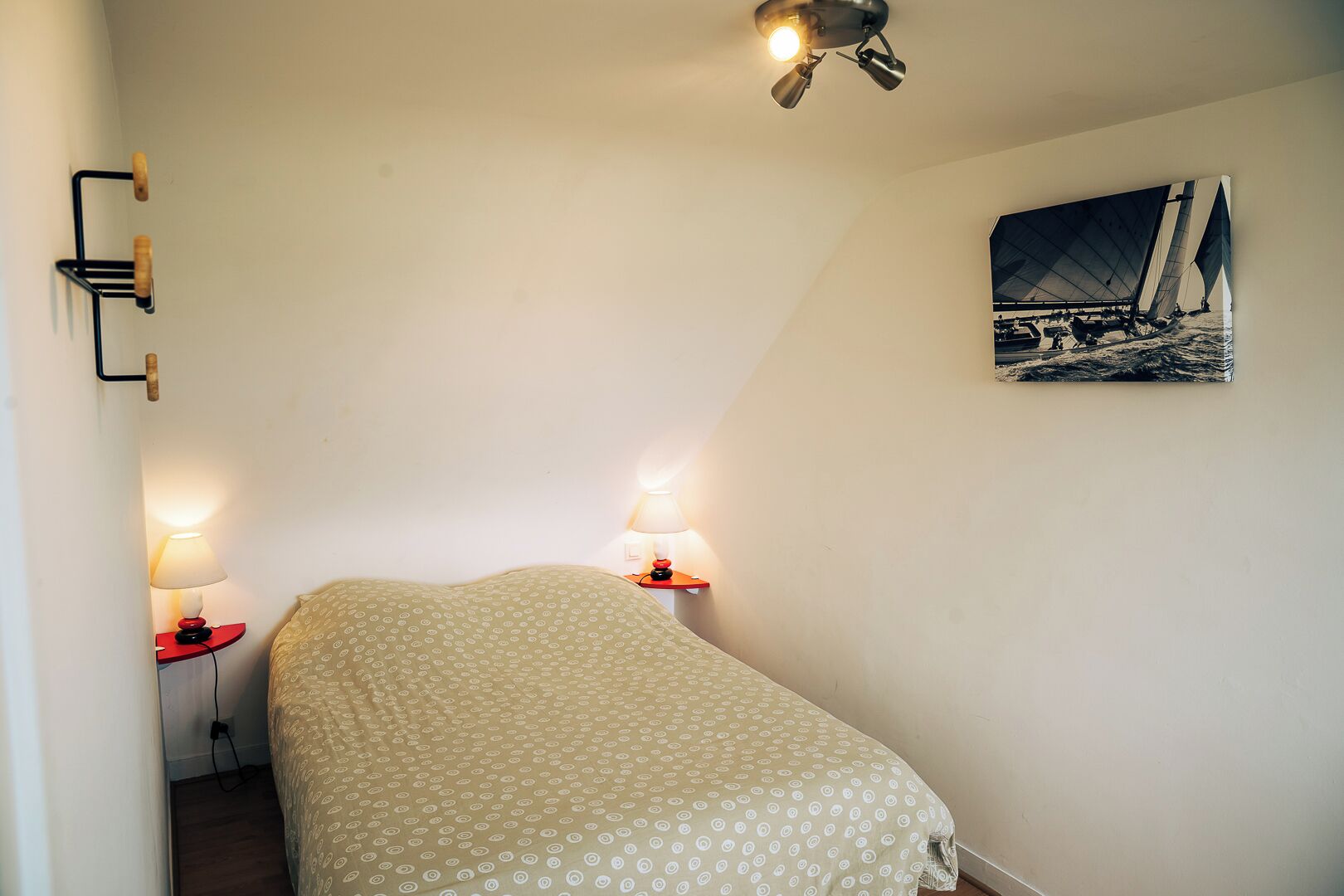 A bedroom with a bed, two bedside lamps, a wall-mounted light fixture, and a sailboat painting.