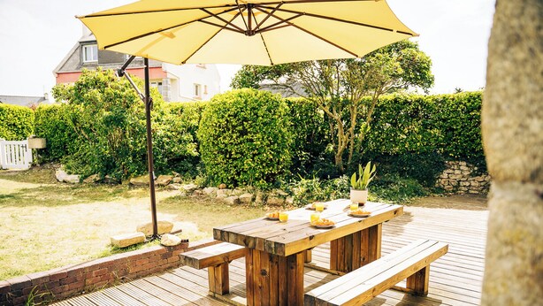 Eine Holzterrasse mit Picknicktisch und Bänken, umgeben von einem Hecken und einer Steinmauer.