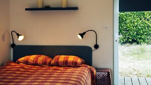 Ein Schlafzimmer mit einem Bett, zwei Nachttischlampen, einem Regal mit Kerzen und Blick auf Grünflächen.