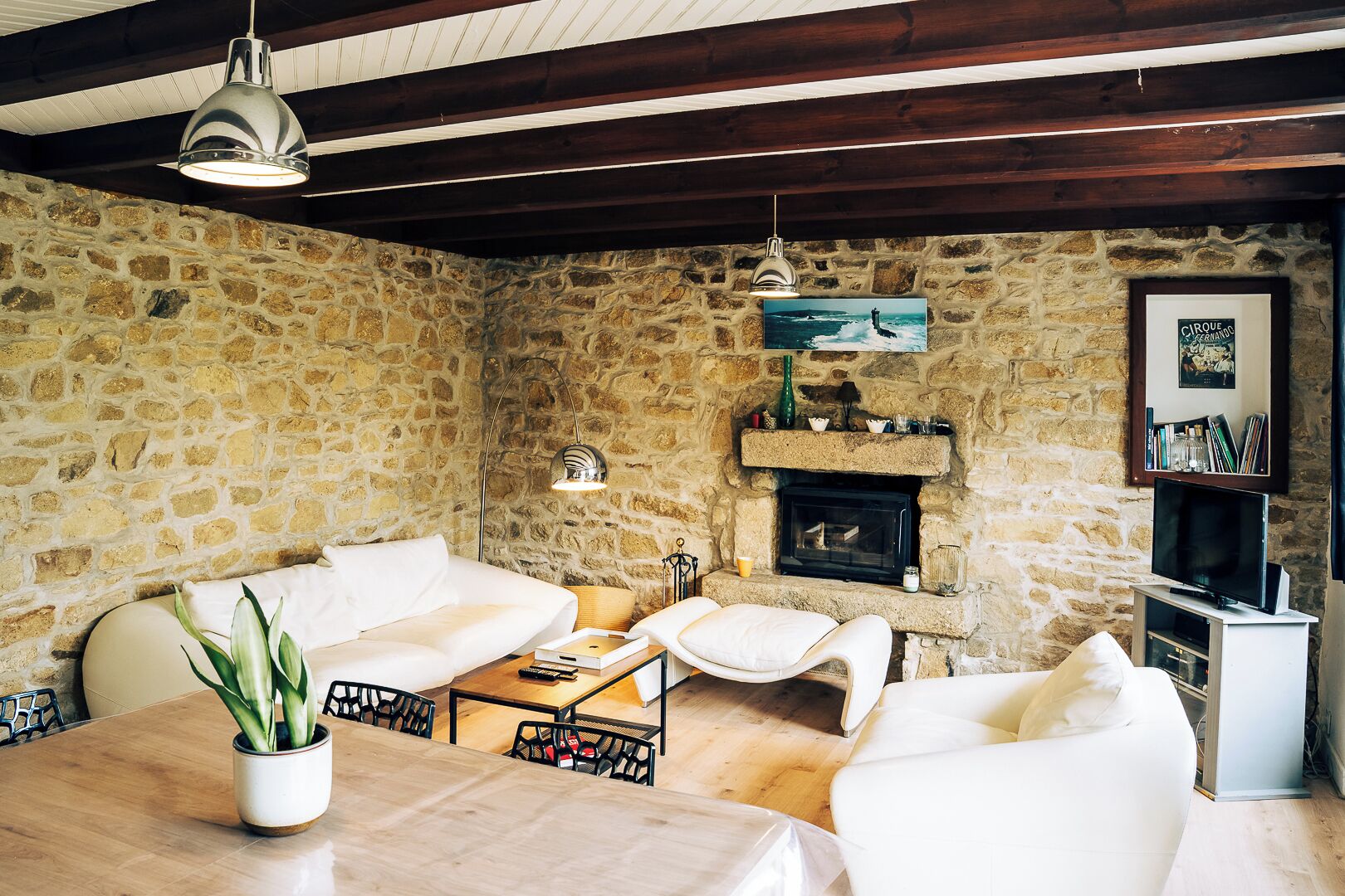 A cozy living room with a stone wall, a fireplace, a white sofa, a dining table, and a TV stand.
