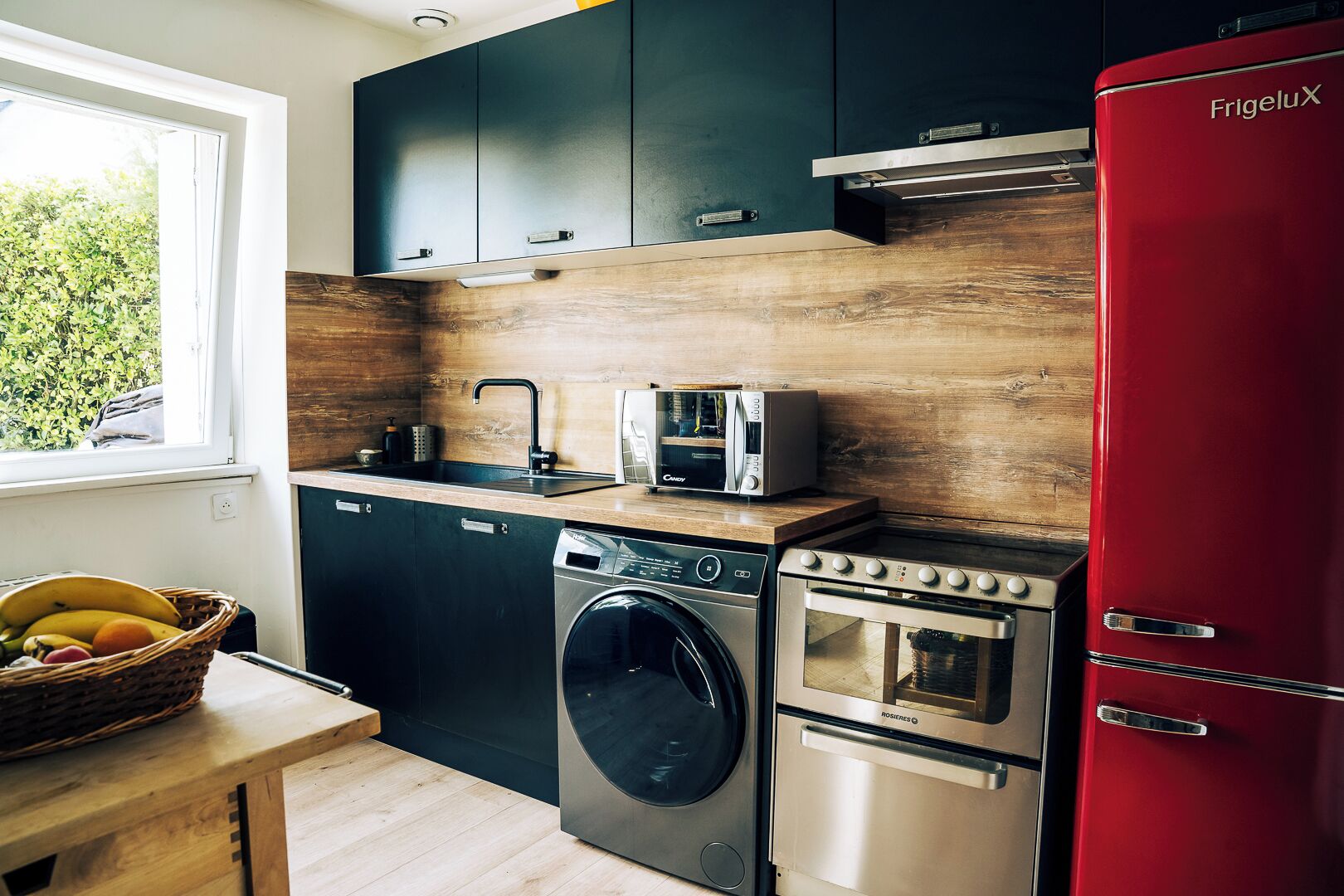 A modern kitchen with a washing machine, a toaster, and a red refrigerator.