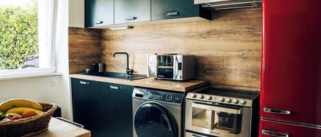 A modern kitchen with a washing machine, a toaster, and a red refrigerator.