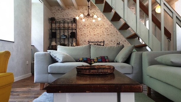 A living room with a light grey sofa, a wooden coffee table, and a staircase with wooden steps and metal railings.