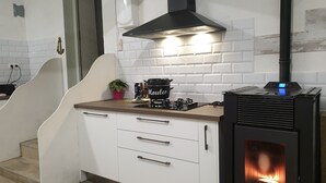 A modern kitchen with white cabinets, a wooden countertop, a black range hood, a gas stove, and a wood-burning stove.