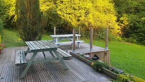 A wooden deck with picnic tables and a raised garden bed with flowers.