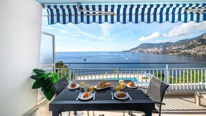 A balcony with a table set for breakfast, overlooking a coastal city and the sea.