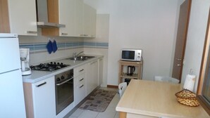 A compact kitchen with white cabinets, a gas stove, a microwave, and a small dining area with a table and chairs. - TOWNHOUSE WITH GARDEN   (Gavazzo  Di Tenno)