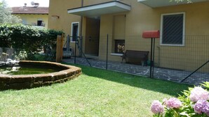 A yellow building with a balcony, a small garden with a fountain, and a bench. - TOWNHOUSE WITH GARDEN   (Gavazzo  Di Tenno)