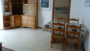 A dining area with a table and chairs, a wooden cabinet with a television, and a kitchen visible through an open door. - TOWNHOUSE WITH GARDEN   (Gavazzo  Di Tenno)