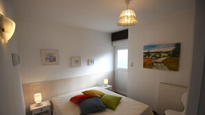 Un dormitorio con cama, lámparas de noche, un radiador y un cuadro en la pared.