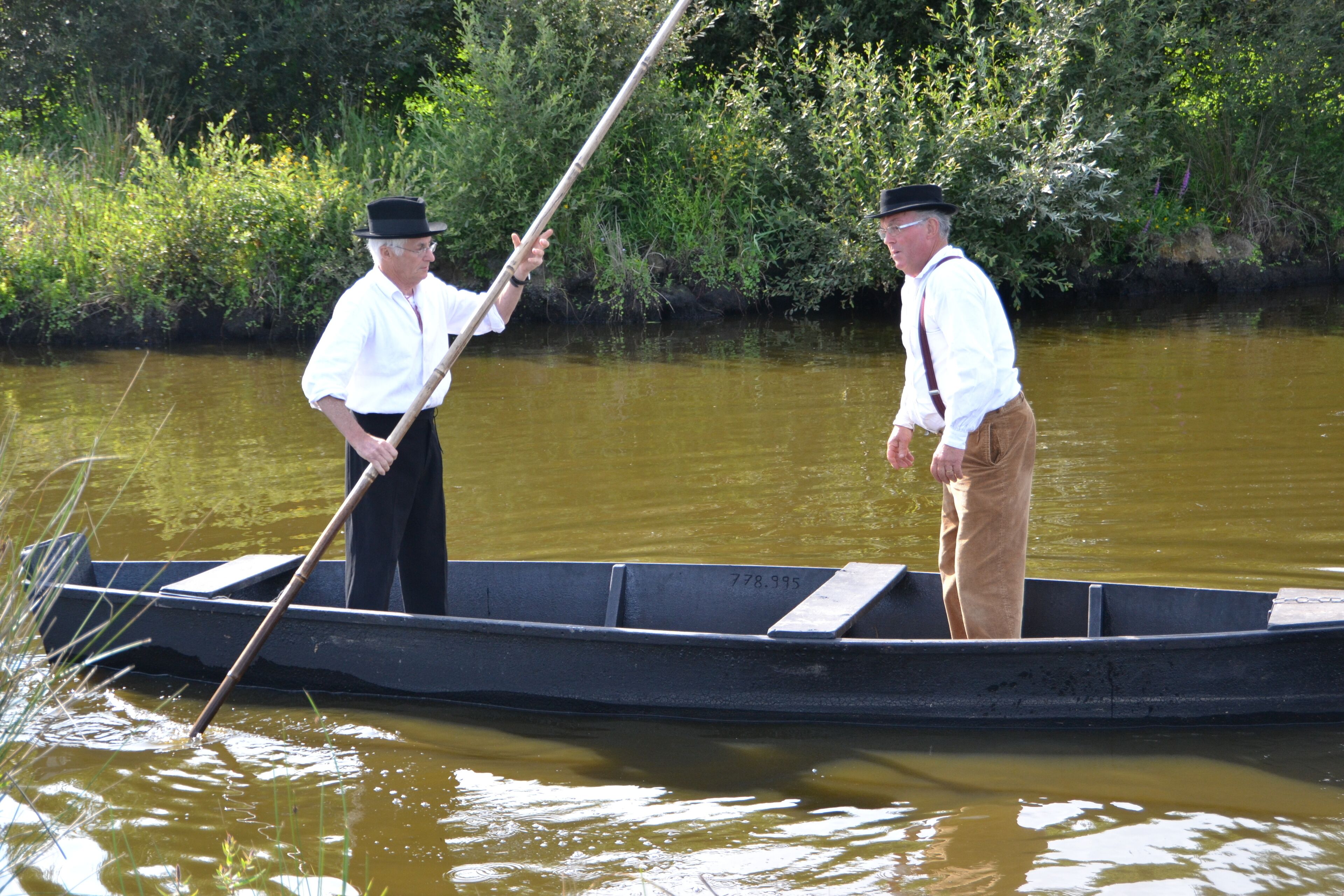 Deux hommes se trouvent dans un petit bateau sur une rivière, et l’un d’eux utilise une rame.