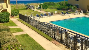 A pool area with lounge chairs and a view of the ocean.