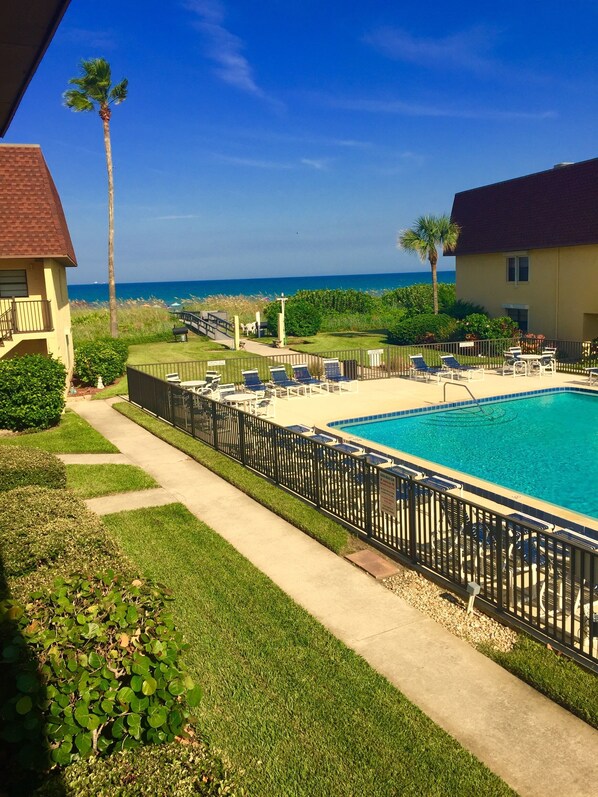 A pool area with lounge chairs and a view of the ocean. - Beachfront 2BR Townhouse Ocean-View Balcony, Pool & Private Beach (Cocoa Beach)