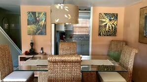 A dining area with wicker chairs, a glass table, and a hanging light fixture.