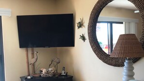 A living room with a flat-screen TV, a woven lamp, decorative items, and a rattan chair.
