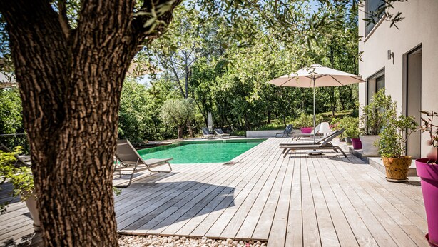 Une terrasse en bois avec une piscine, des chaises longues et une table avec un parasol.