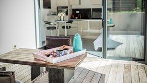Un coin repas avec un plateau de nourriture, une table en osier et une vue sur une cuisine moderne et un espace extérieur.