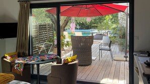 Une pièce dotée d’une porte-fenêtre coulissante donnant sur une terrasse extérieure avec un parasol rouge, des meubles en osier et une piscine.