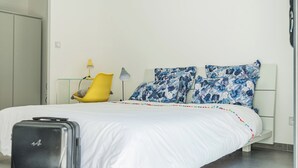 Une chambre à coucher avec un lit, une valise, une chaise et une lampe.