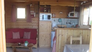 A cozy cabin interior with a wooden interior, a red sofa, a small kitchen area with a microwave, and a dining table. - Chalet Le Serre (Chorges)
