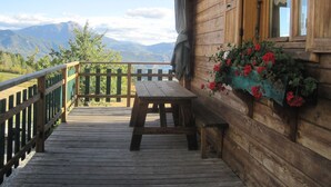A wooden deck with a picnic table and benches, overlooking a mountainous landscape. - Chalet Le Serre (Chorges)