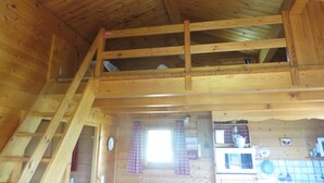 A wooden cabin interior with a loft bedroom, a kitchen area, and a visible window. - Chalet Le Serre (Chorges)