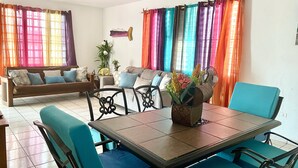 A dining area with a table and chairs, a sofa, and colorful curtains. - Villa Caribe by Casa Caribe Vacation Rentals (Aguadilla)