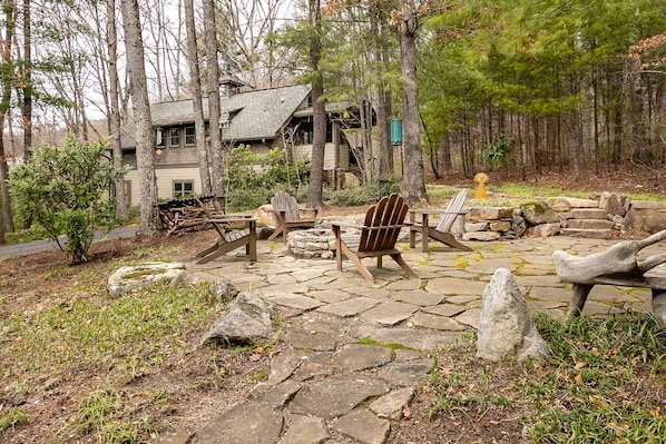 Un chalet rustique doté d’un patio en pierre, de fauteuils Adirondack en bois et d’un foyer extérieur.