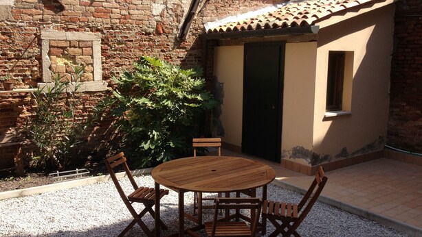 A small outdoor patio with a wooden table and chairs, surrounded by gravel.