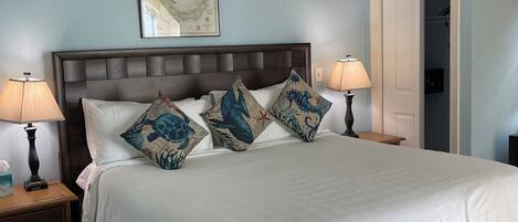 A bedroom with a large bed, two bedside tables, a ceiling fan, and a door leading to another room.