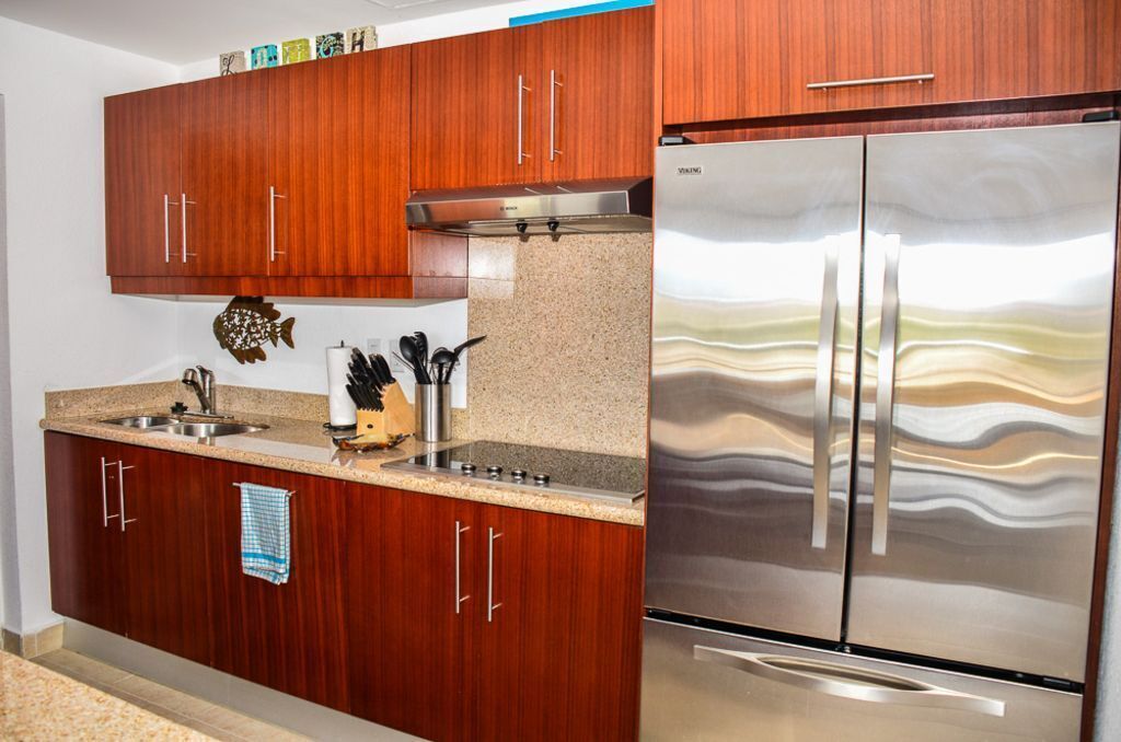 A modern kitchen with wooden cabinets, a stainless steel refrigerator, and granite countertops.