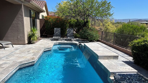 Une piscine rectangulaire agrémentée d’une cascade, entourée d’une terrasse avec des chaises et une clôture.