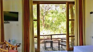 A room with a wooden bench and table, a television on the wall, and a view of greenery outside. - Hotel Saji-Sami (Mihintale)