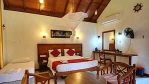 A hotel room with a wooden ceiling, a bed with red pillows, a wooden dining table with chairs, a ceiling fan, and a wall-mounted air conditioner. - Hotel Saji-Sami (Mihintale)