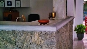 A stone counter with a bowl and a brass container, a potted plant, and a wall with framed certificates. - Hotel Saji-Sami (Mihintale)