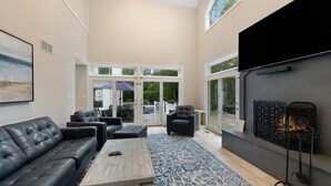 A spacious living room with a fireplace, leather sofas, a coffee table, and a large window overlooking a patio. - "New" Lake Michigan R & R Recently Completed Major Rehab (Union Pier)