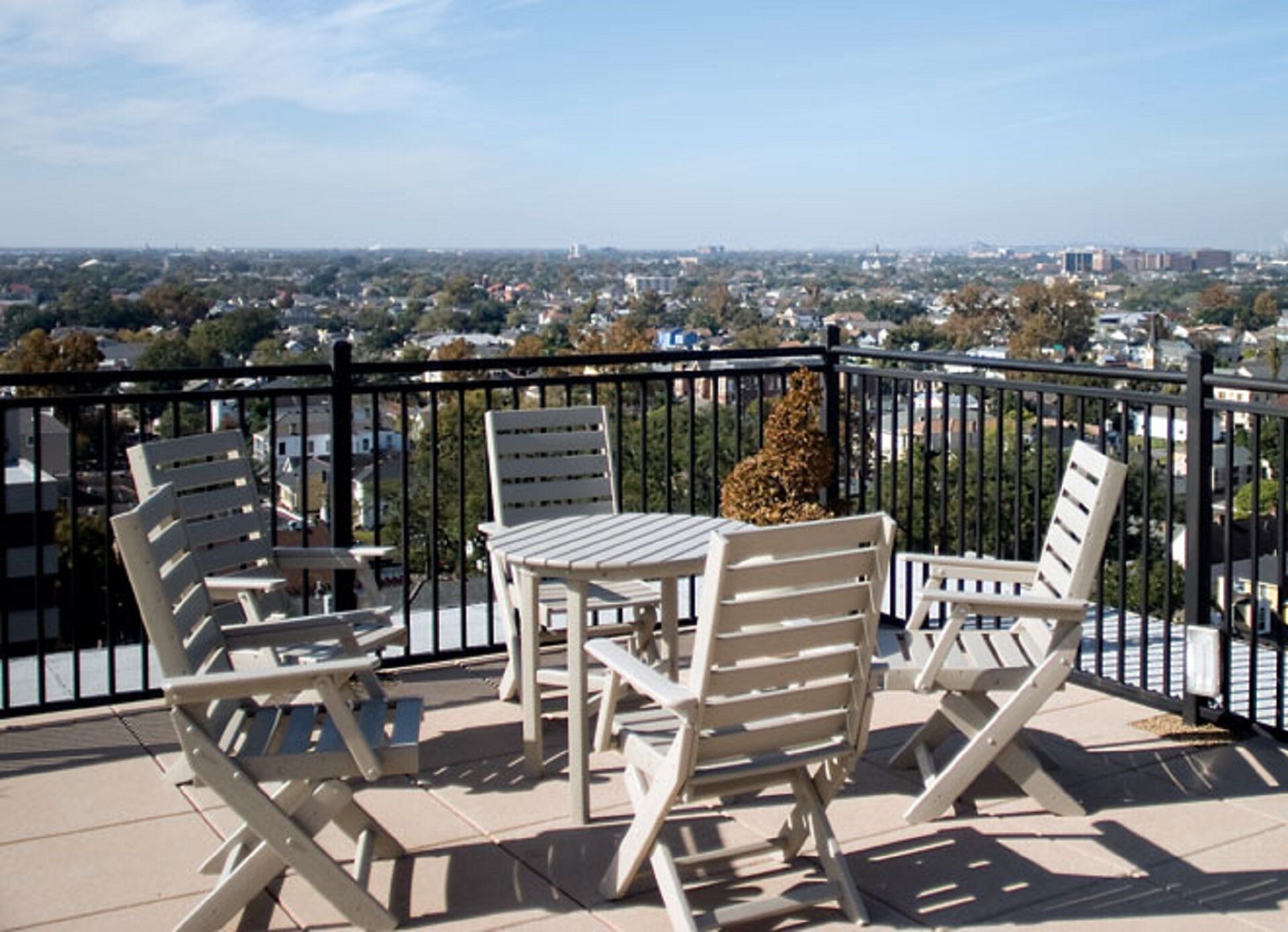 A balcony with white chairs and a table, offering a view of a cityscape.