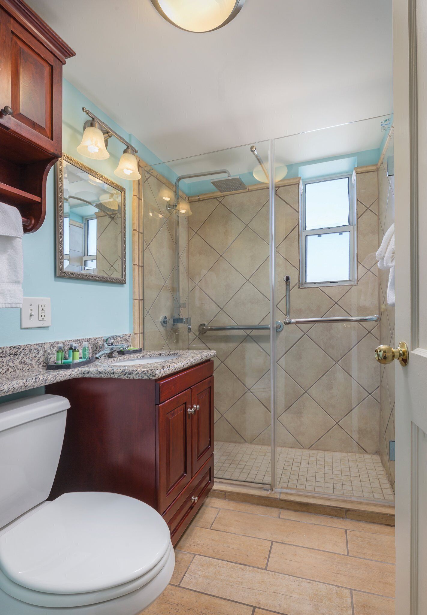 A bathroom with a toilet, sink, vanity, and a glass-enclosed shower area.