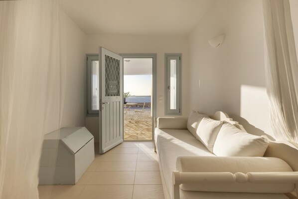 Une pièce avec un canapé beige, un petit meuble et une porte donnant sur la plage.