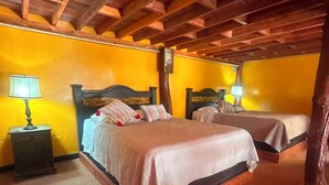 Ein Zimmer mit zwei Betten, Holzbalken an der Decke und einer gelben Wand.