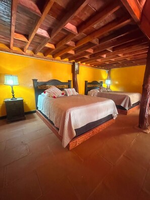 Une chambre avec deux lits, des poutres en bois au plafond et un mur jaune.