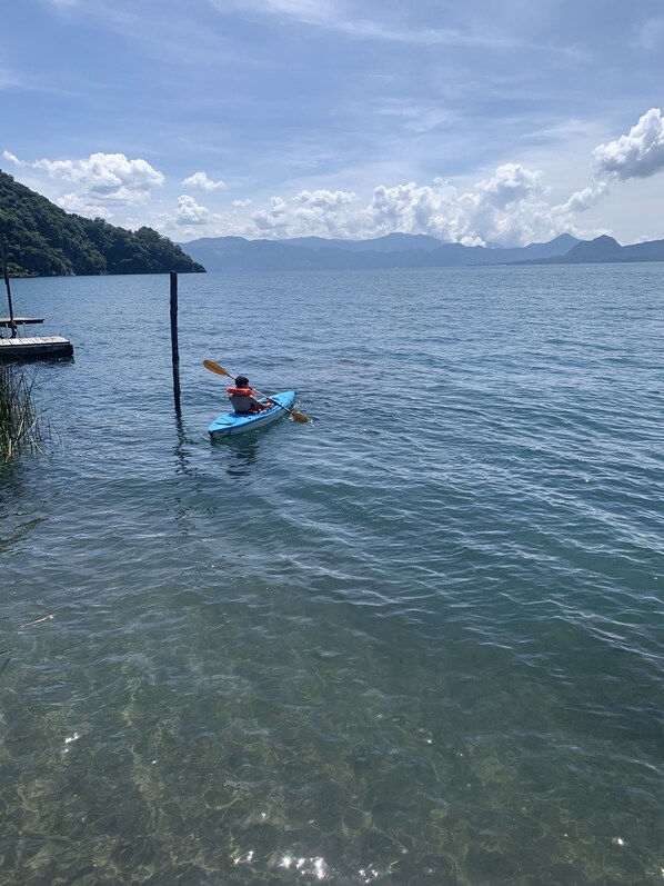 A kayaker in a blue kayak on a calm lake with clear water, surrounded by mountains and a dock on the left. - hotel cabanas de tzununa is located in lake atitlan (Santa Cruz Laguna)