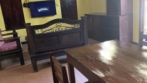 Ein Zimmer mit einem Holztisch, Stühlen, einem an der Wand montierten Fernseher, einer Couch und einem Schrank.