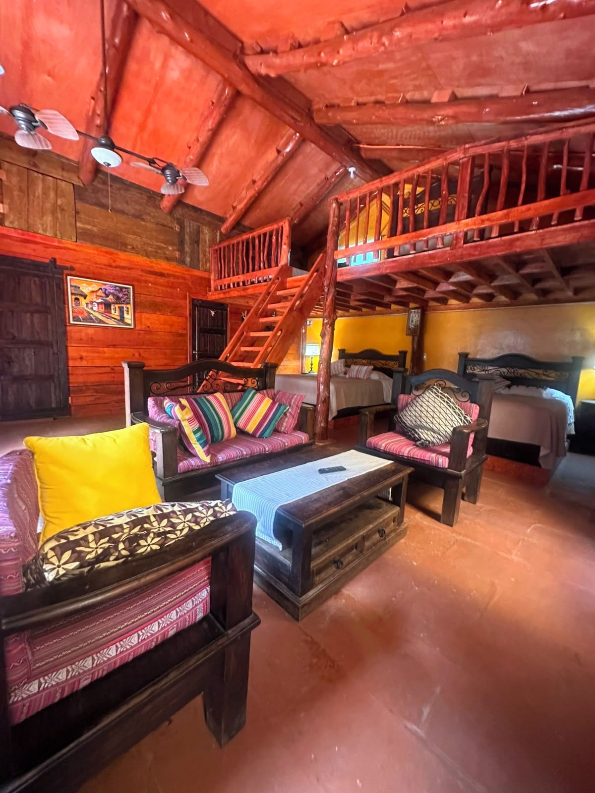 Une pièce rustique avec des murs en bois, un escalier, un ensemble de meubles de salon et un lit.