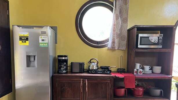 Eine kompakte Küche mit Kühlschrank, Kaffeemaschine, Wasserkocher, Mikrowelle und einer kleinen Ablage für Geschirr.