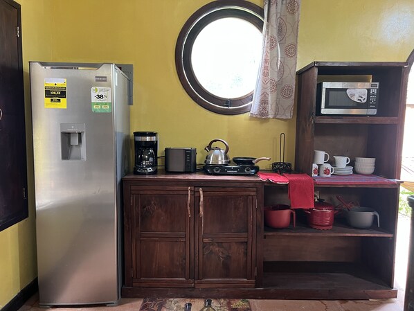 Une cuisine compacte équipée d’un réfrigérateur, d’une machine à café, d’une bouilloire, d’un four à micro-ondes et d’une petite étagère avec de la vaisselle.