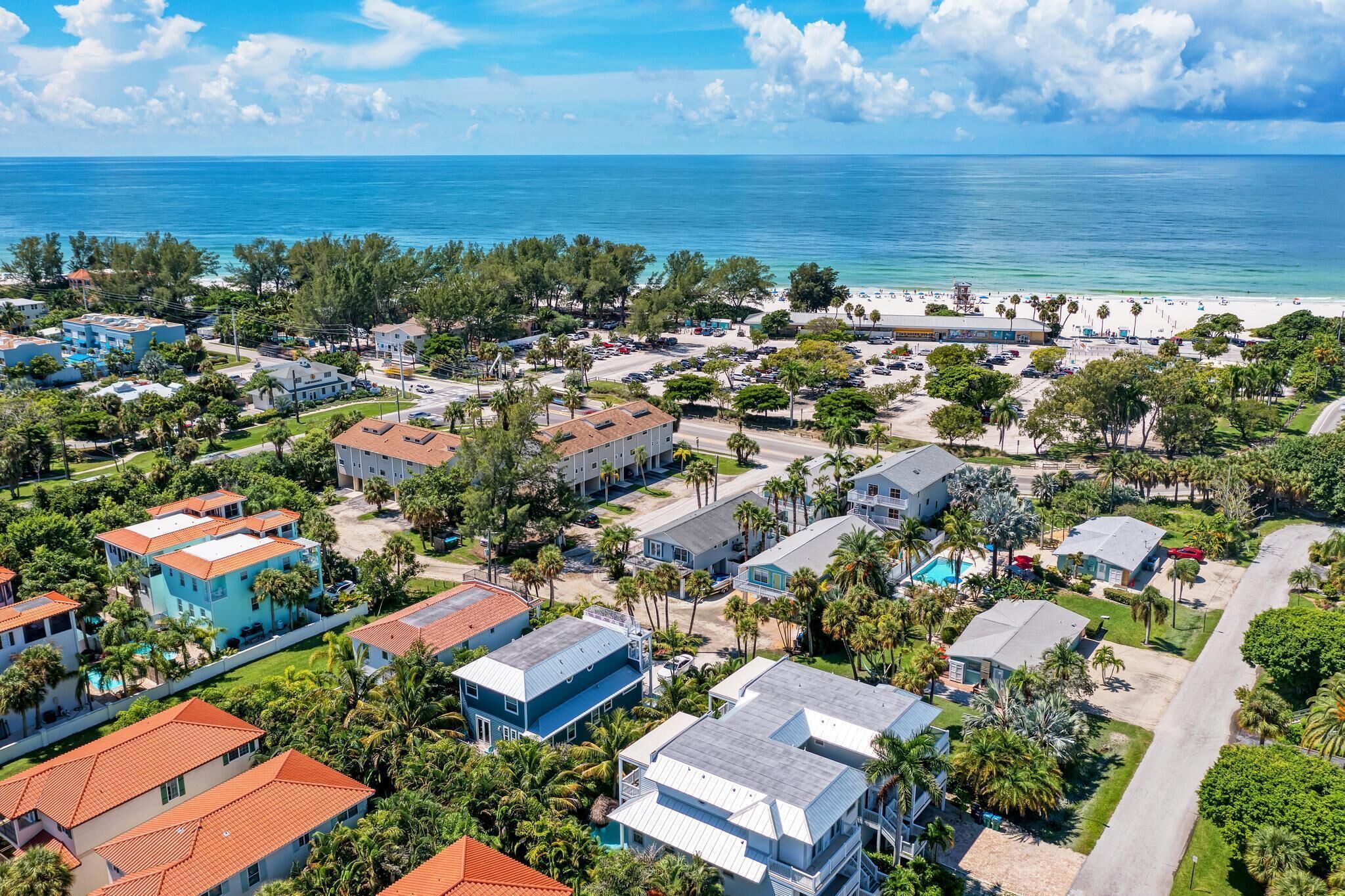 An aerial view of a coastal residential area with houses, a beach, and a clear blue sky.