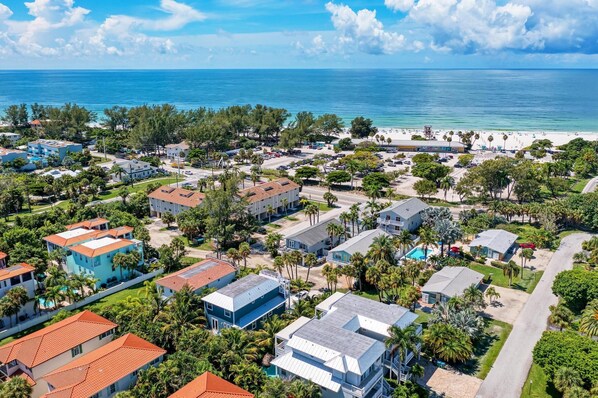 An aerial view of a coastal residential area with houses, a beach, and a clear blue sky.